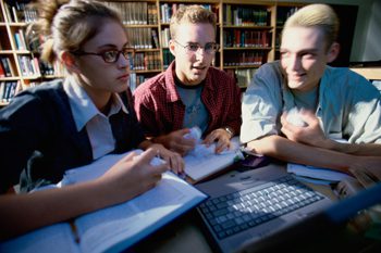 A group of students working on a laptop in a library.