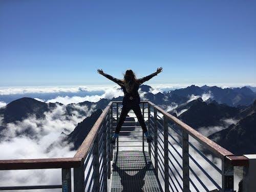 Person standing with arms outstretched on a mountain viewpoint above the clouds.