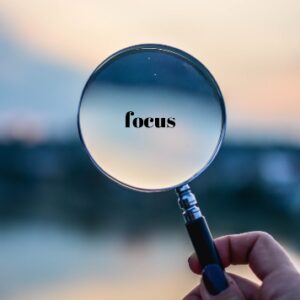 Hand holding a magnifying glass with the word "focus" visible through the lens.